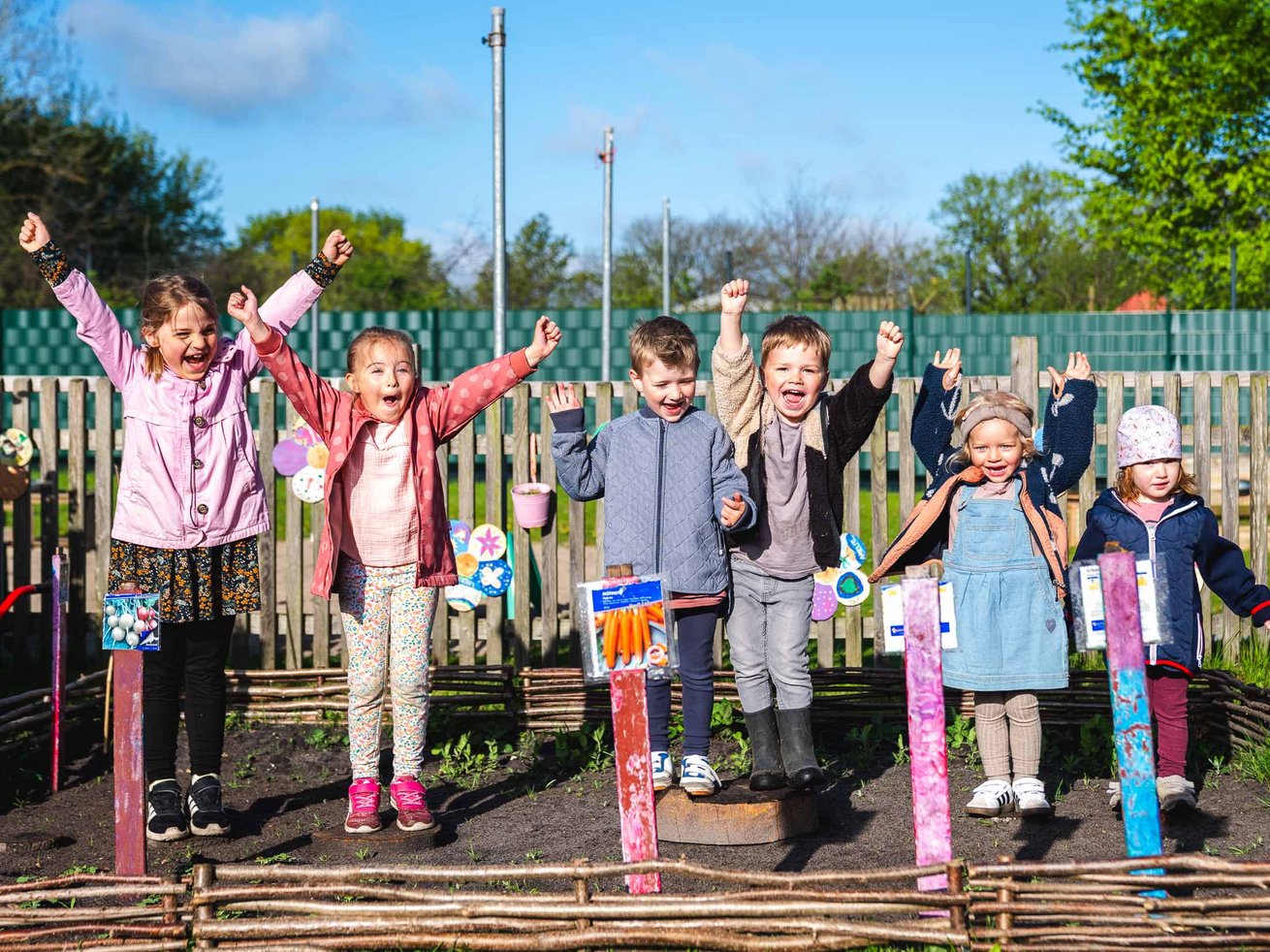 Gruppe von Kindern mit erhobenen Armen im Außengelände der Kita.