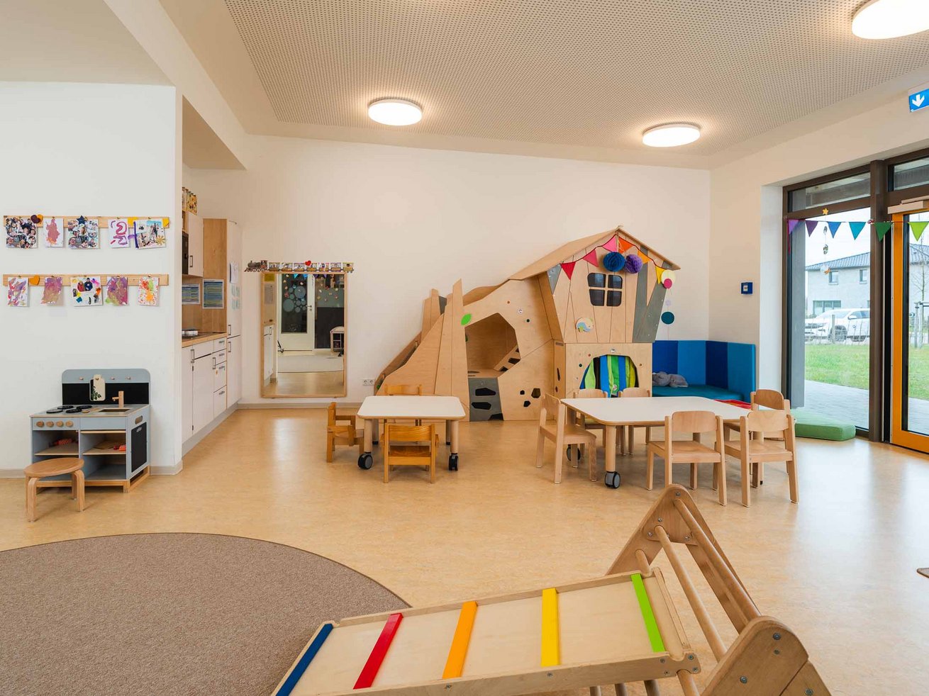 Spiel- und Gruppenraum der Kita mit Spielhaus, Tischen und Kinderküche.
