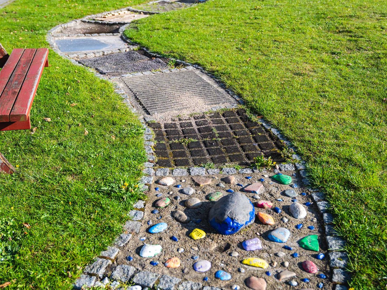 Barfußpfad im Garten der Kita mit unterschiedlichen Materialien, Steinen und Naturflächen.