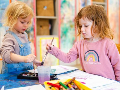 Zwei Kinder malen gemeinsam mit Pinseln und Wasserfarben in einem Kreativraum der Kita.