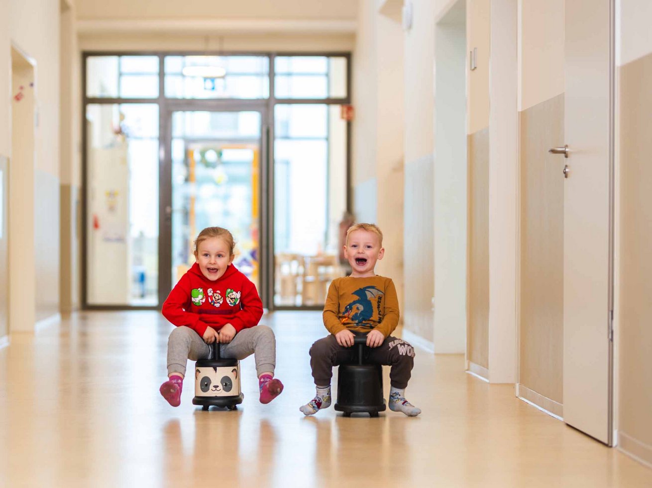 Zwei Kinder auf Rutschfahrzeugen im Flur der Kita.