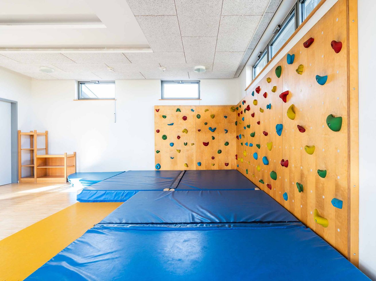 Kletterbereich der Sport-Kita mit großer Kletterwand und blauen Fallschutzmatten.