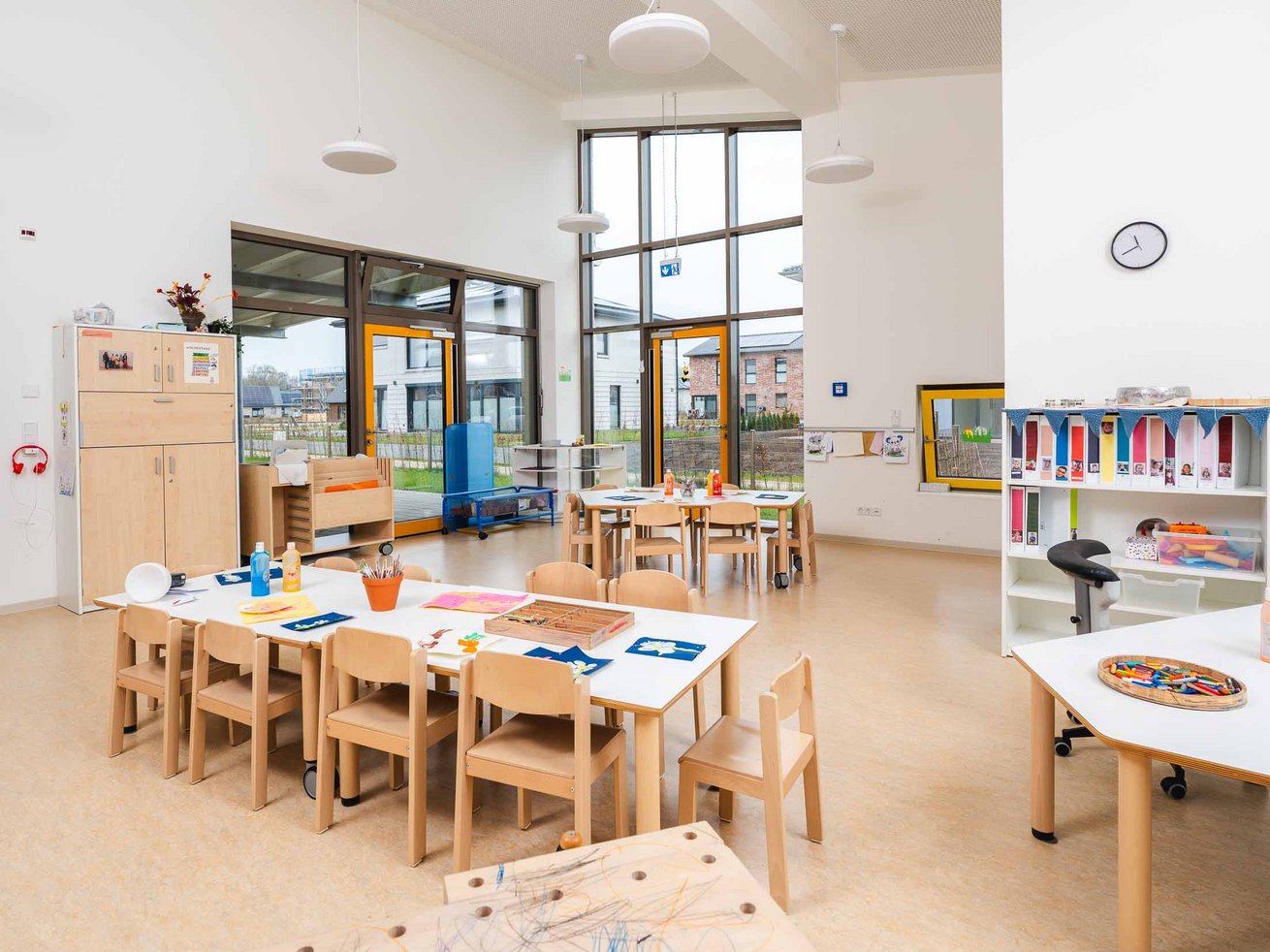 Heller Gruppenraum der Kita Anne-Frank-Ring mit Kindertischen, Stühlen und großen Fenstern.