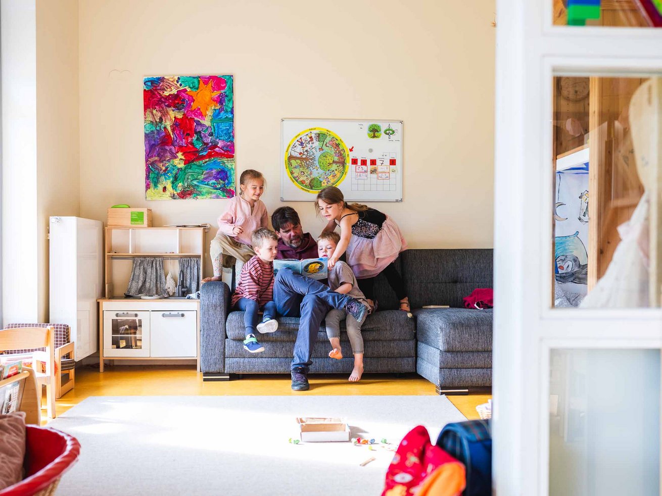 Erzieher liest mehreren Kindern auf einem Sofa vor.