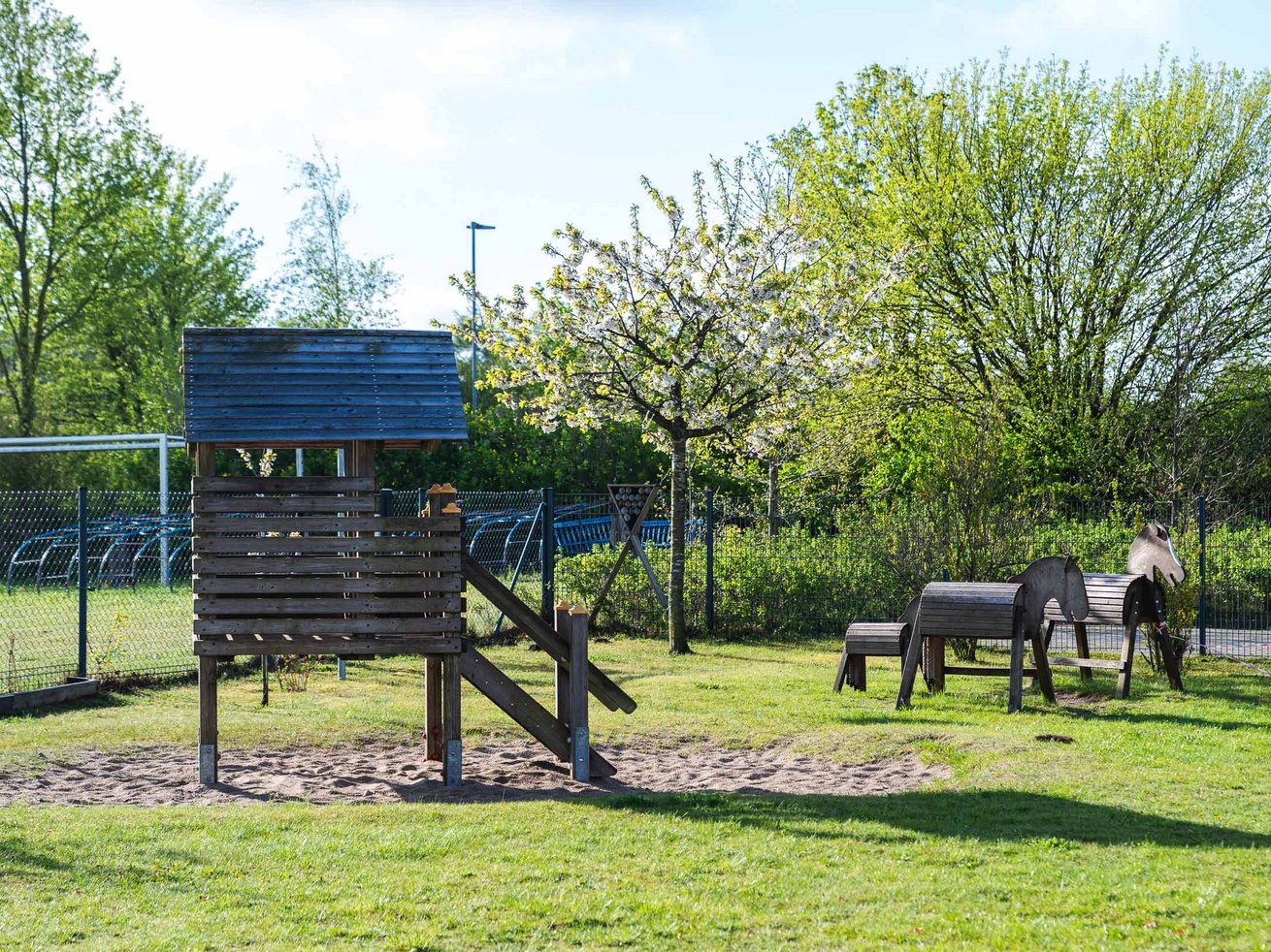 Naturnaher Spielbereich im Außengelände der Kita mit Holzspielhaus und Holzpferden.