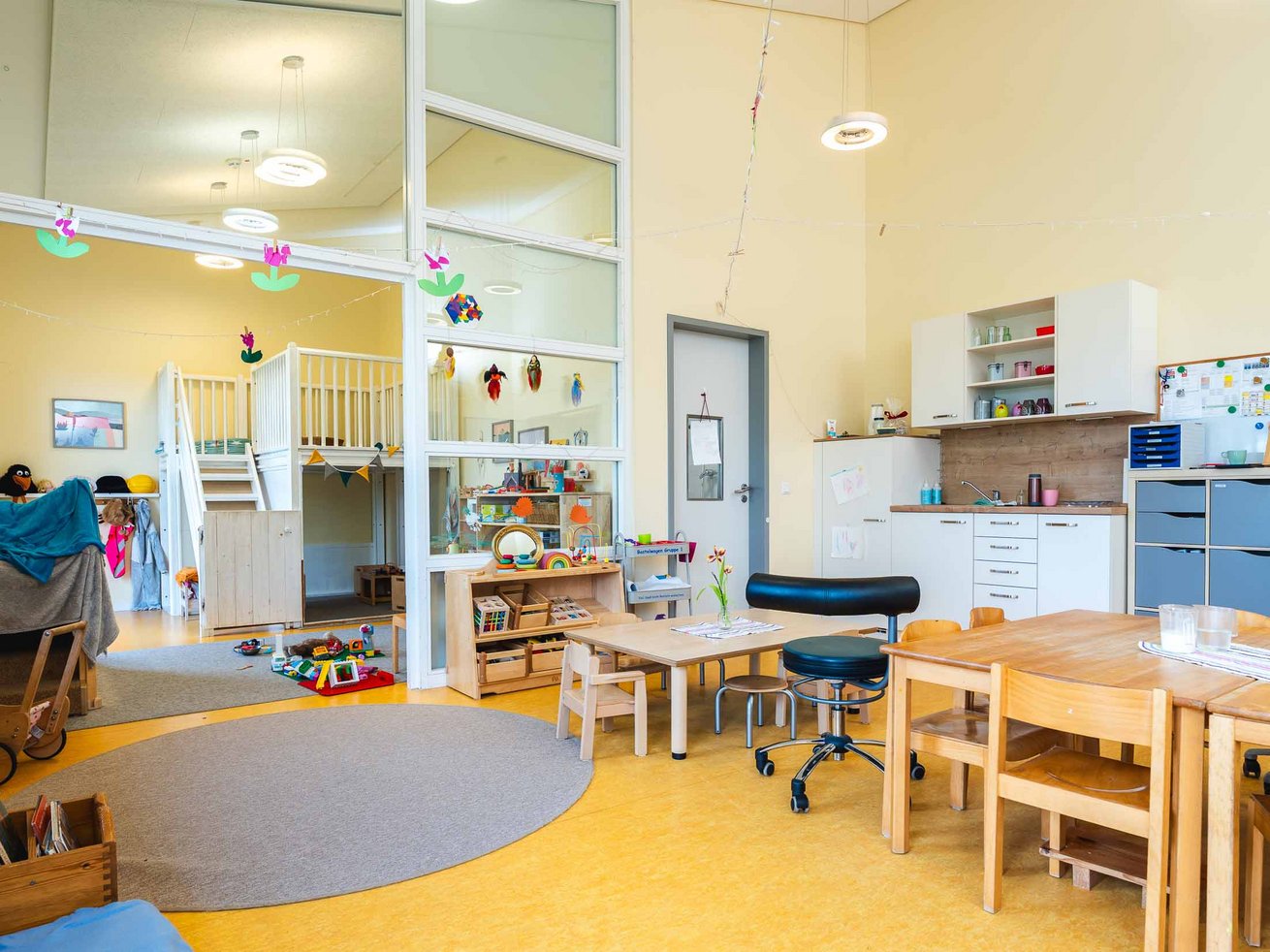 Gruppenraum der Kita mit Spielbereich, Kinderküche, Tischen und verschiedenen Spielmaterialien.