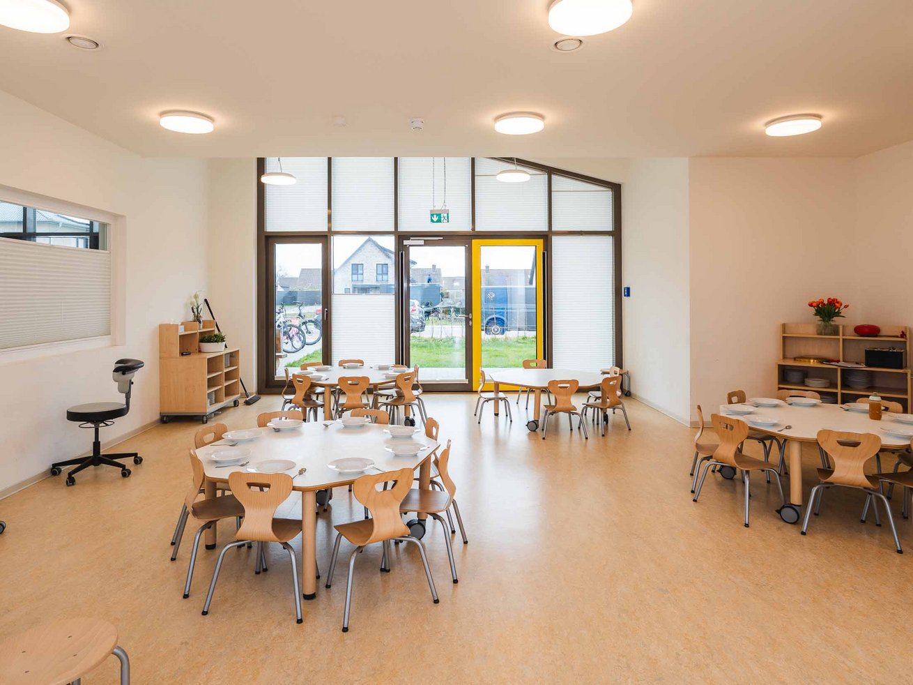 Heller Essbereich mit mehreren gedeckten Kindertischen.