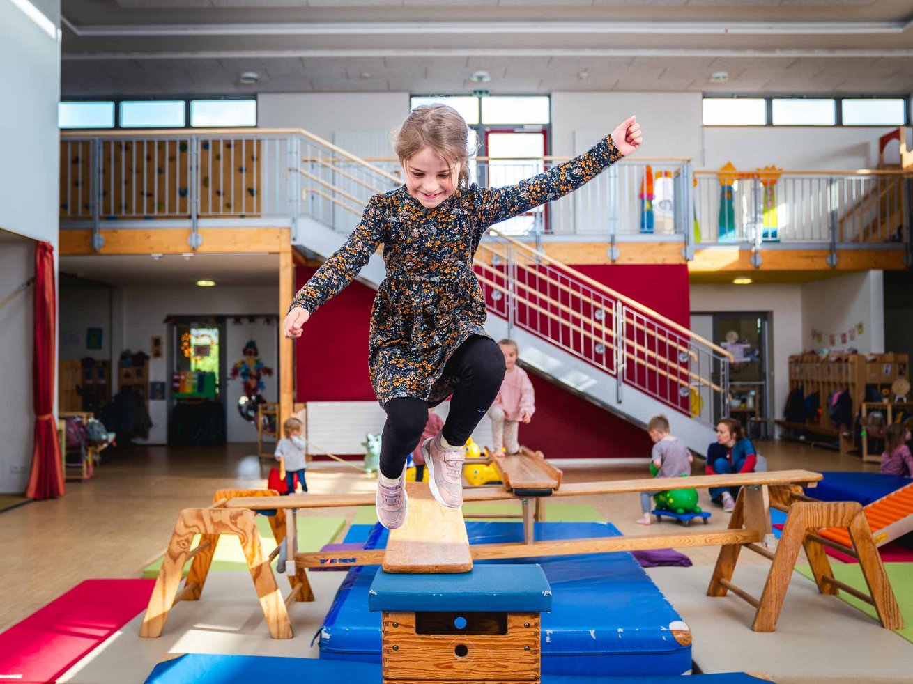 Mädchen springt über einen Bewegungsparcours mit Turngeräten und Matten in der Sport-Kita.